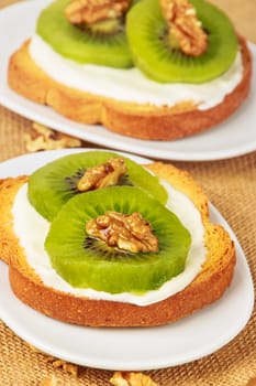 Toast with kiwi, cheese and walnuts on a piece of sackcloth with walnuts around.