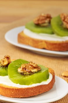 Toast with kiwi, cheese and walnuts on a piece of sackcloth with walnuts around.