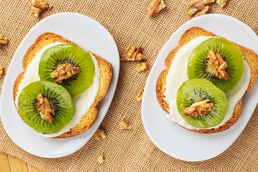 Toast with kiwi, cheese and walnuts on a piece of sackcloth with walnuts around. View from above 