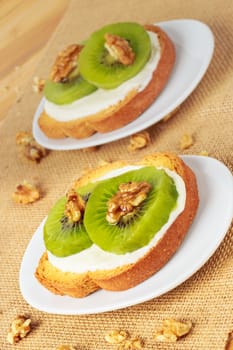 Toast with kiwi, cheese and walnuts on a piece of sackcloth with walnuts around.