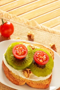 Toast with kiwi, cheese and cherry tomato on a piece of sackcloth in wooden board.