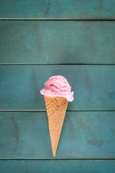 Top view pink ice cream in waffle cone on blue rustic wooden background.