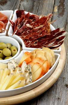 Various Spanish Snacks with Goat Cheeses, Jamon, Cured Ham and Green Olives on Serving Plate closeup on Wooden background