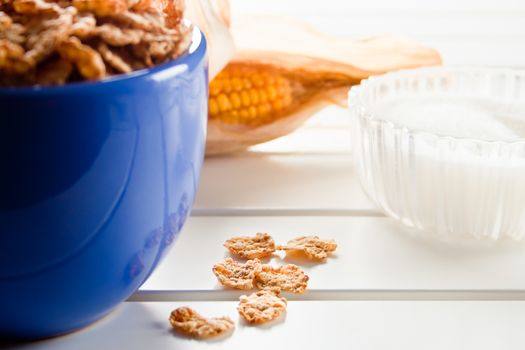 Cornflakes in a blue bowl on white wooden table with cob and sugar