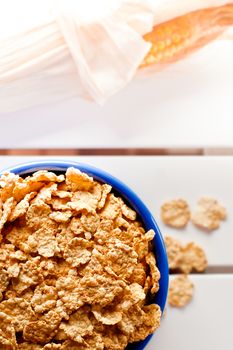 Cornflakes in a blue bowl on white wooden table with a cob