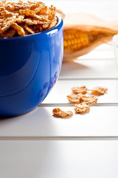 Cornflakes in a blue bowl on white wooden table with a cob