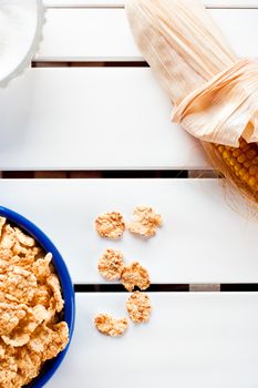 Cornflakes in a blue bowl on white wooden table with cob and sugar