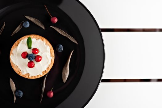 Cookies with cream cheese and blueberries in a dark plate surrounded with berries and dry leaves