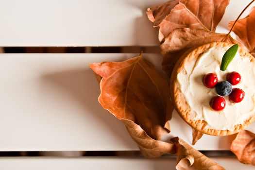 Cookies with cream cheese, blueberries and dry autumn leaves around in a white table