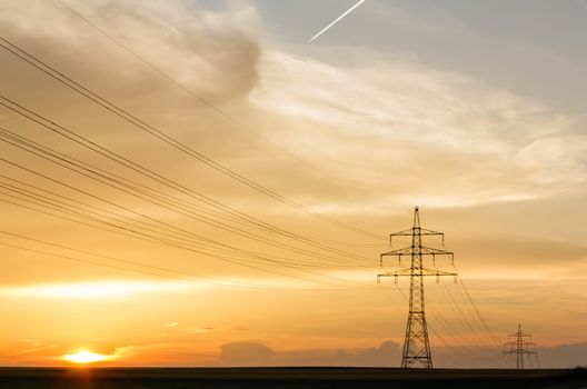 transmission line with poles in front of a yellow and amber sky at sunset or sunrise with condensation trail transmission line and sunrise