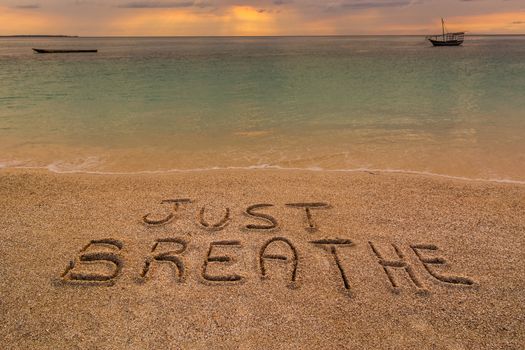 In the picture a beach at sunset with the words on the sand "Just breathe".