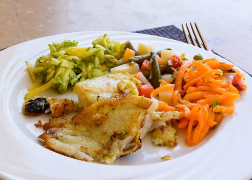 In the picture a fried fish fillet with vegetables served on white dish at the restaurant.