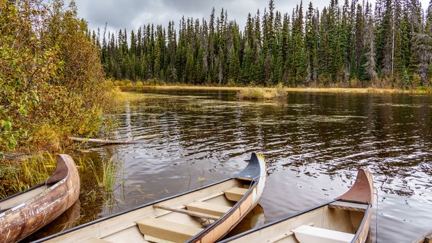 Canoes moored in McGillivray Lake in the Shuswap Highlands in central British Columbia with surrounding trees reflecting on the water