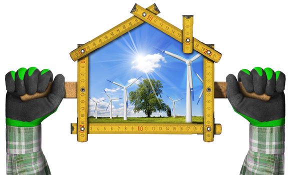 Hands with work gloves holding a wooden meter ruler in the shape of house with wind turbines in countryside with tree, blue sky, clouds and sun rays.