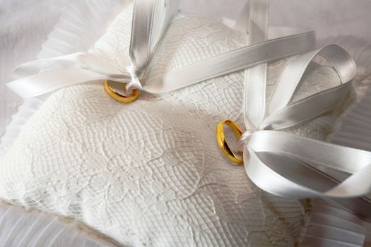 yellow gold wedding rings on white pillow with tassels