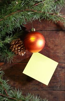 Christmas decoration. Pinecones and glass ball near empty sticky note on old wooden background