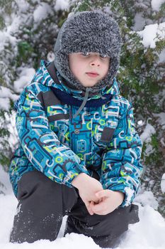 A boy sits near a Christmas tree in the snow