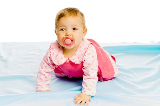 Beautiful baby girl with pacifier crawling on the blue coverlet. Studio