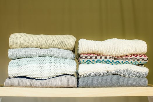 Two piles of warm sweaters for fall or winter on a shelf in a closet. Soft draped background.