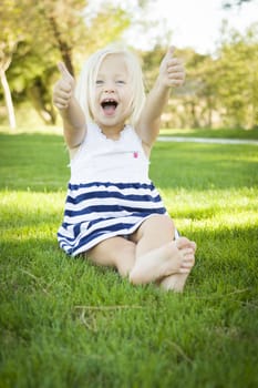 Cute Little Girl with Thumbs Up in the Grass Outside.