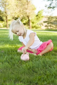 Cute Little Girl Having Fun with Her Piggy Bank Outside on the Grass.