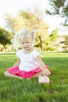 Cute Little Girl Having Fun with Her Piggy Bank Outside on the Grass.