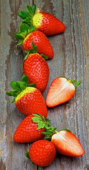 Raw Ripe Strawberries Full Body In a Row and Halves isolated on Textured Wooden background