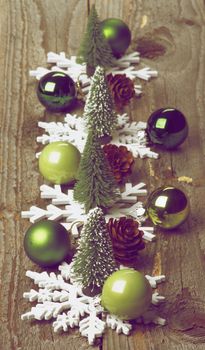 Little Christmas Trees, Green Baubles, Decorative Fir Cones and Snowflake Shapes In a Row on Rustic Wooden background. Retro Styled