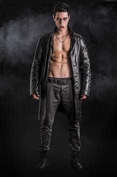 Portrait of a Young Vampire Man in an Open Black Leather Jacket, Showing his Chest and Abs, Looking at the Camera, on Black Background.