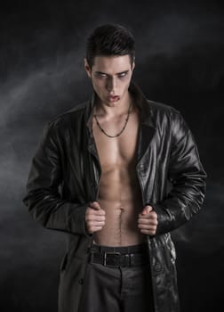 Portrait of a Young Vampire Man in an Open Black Leather Jacket, Showing his Chest and Abs, Looking at the Camera, on Black Background.
