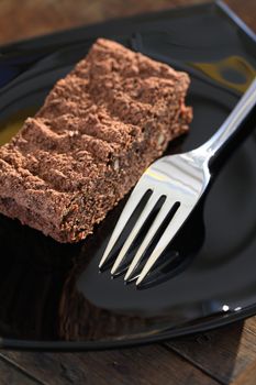 One piece of chocolate pie near fork on black glass plate