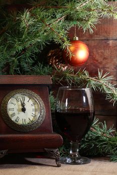 Vintage clock near glass of red wine on old wooden background with Christmas decoration