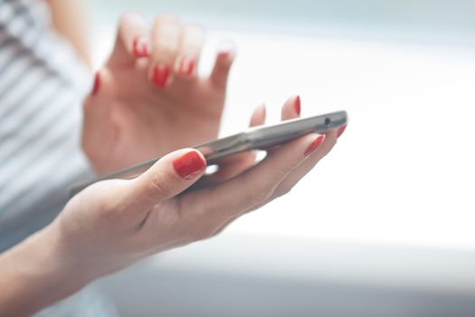 Woman with red manicure using smartphone. Horizontal photo