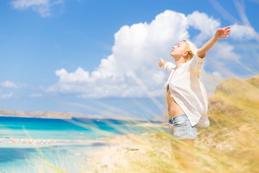 Relaxed woman enjoying freedom and life an a beautiful sandy beach.  Young lady raising arms, feeling free, relaxed and happy. Concept of freedom, happiness, enjoyment and well being.