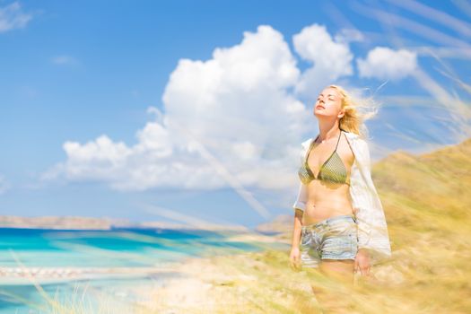 Relaxed woman enjoying freedom and life an a beautiful sandy beach.  Young lady feeling free, relaxed and happy. Concept of freedom, happiness, enjoyment and well being.  Enjoying Sun on Vacations.