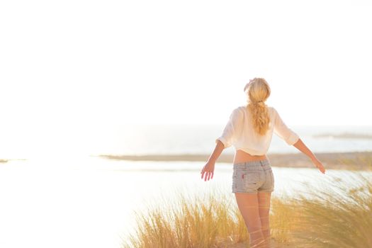 Relaxed woman enjoying freedom and life an a beautiful sandy beach.  Young lady feeling free, relaxed and happy. Concept of happiness, enjoyment and well being.  Enjoying Sun on Vacations. Copyspace.