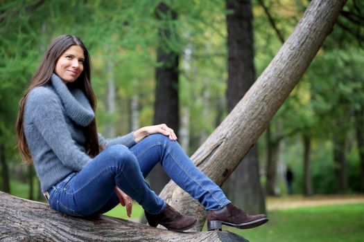 Beautiful brunette woman sitting on tree in park