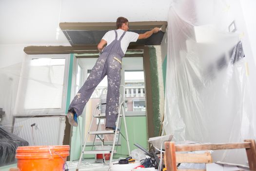 Thirty years old manual worker with wall plastering tools inside a house. Plasterer renovating indoor walls and ceilings with float and plaster.