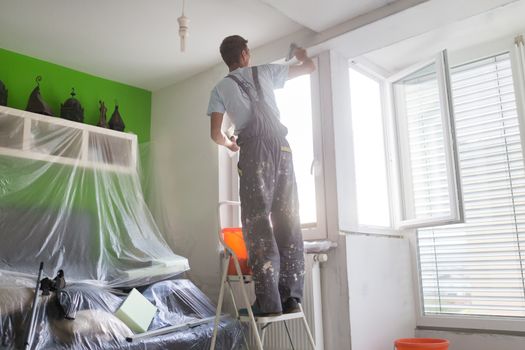 Thirty years old manual worker with wall plastering tools inside a house. Plasterer renovating indoor walls and ceilings with float and plaster.