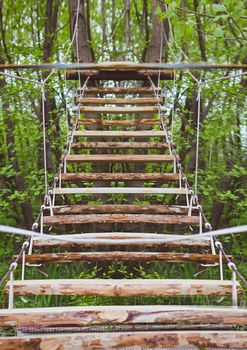 Wooden stairs in the green forest park with ropes