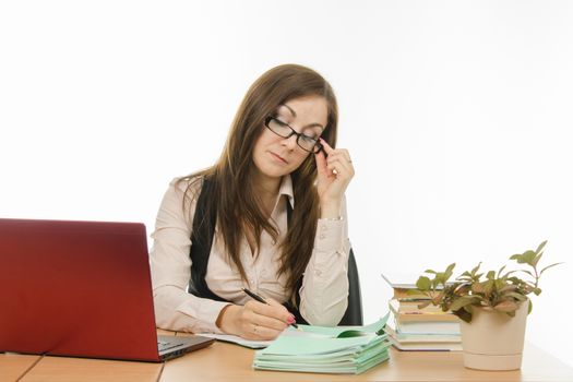 Cute little girl is a teacher sitting at a desk with a laptop, books and notebooks