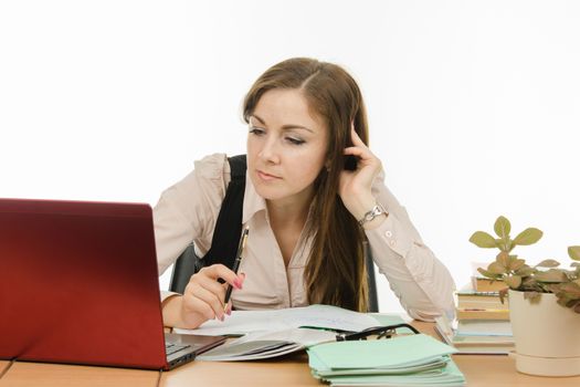 Cute little girl is a teacher sitting at a desk with a laptop, books and notebooks