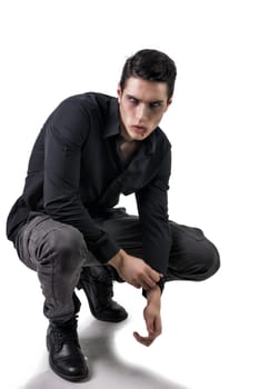Portrait of a Young Vampire Man with Black Shirt Sitting on Floor with Hands Joined, Isolated on White