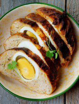 Delicious Slised Meatloaf Stuffed with Boiled Eggs in Bowl closeup on Rustic Wooden background