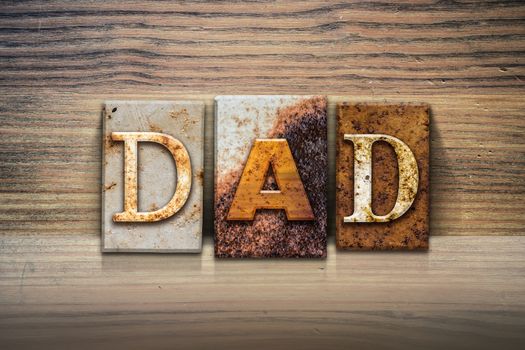 The word "DAD" written in rusty metal letterpress type sitting on a wooden ledge background.