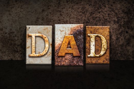 The word "DAD" written in rusty metal letterpress type on a dark textured grunge background.