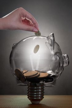 Money being put into a glass light bulb in the shape of a piggybank 