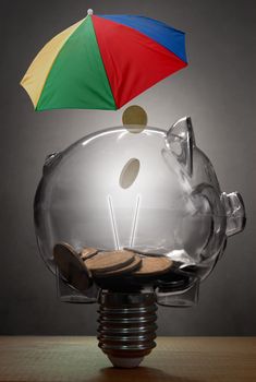 Piggy bank in the shape of a light bulb underneath an umbrella 