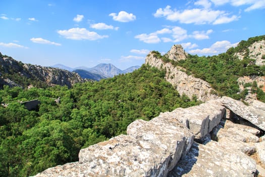 View of high mountains with small floiage and rocks around, on cloudy blue sky background.
