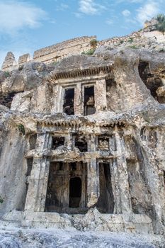 View of abandoned and destroyed rock tombs of Tlos Ancient City, on cloudy blue sky background.